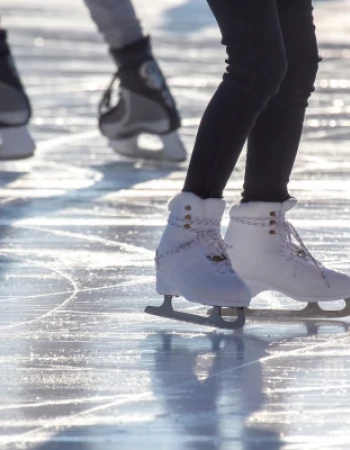 Two people ice skating on a rink, one wearing white figure skates and the other wearing black hockey skates.